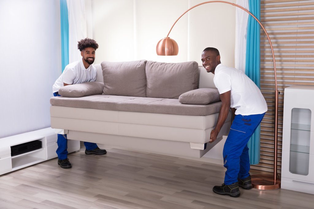 Two Young Male Movers In The White Uniform Placing The Sofa In The Living Room